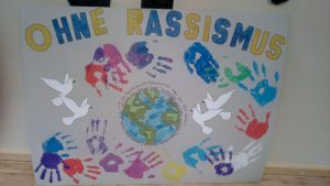 Selbst gestaltetes Plakat von Schüler*innen für "Schulen ohne Rassismus - Schulen mit Courage" (SOR-SMC) zeigt Titel, Welt, tauben und Handabdrücke in bunten Farben.