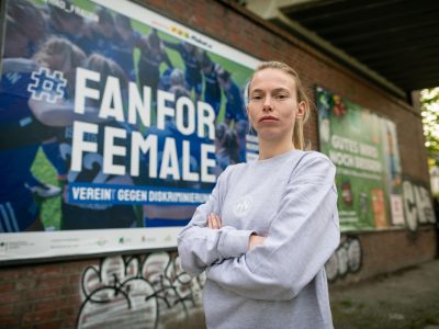 Die Fotoaufnahme zeigt eine Fußballerin vom SV Blau-Weiss Hohen Neuendorf e. V. vor der Plakatkampagne #fanforfemale