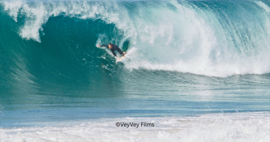 Das Bild zeigt eine im Meer surfende Person. Ein Still von ©VeyVey Films zur Bewerbung der Filmvorführung "Surf on, Europe" im Rahmen der Internationalen Wochen gegen Rassismus 2026.